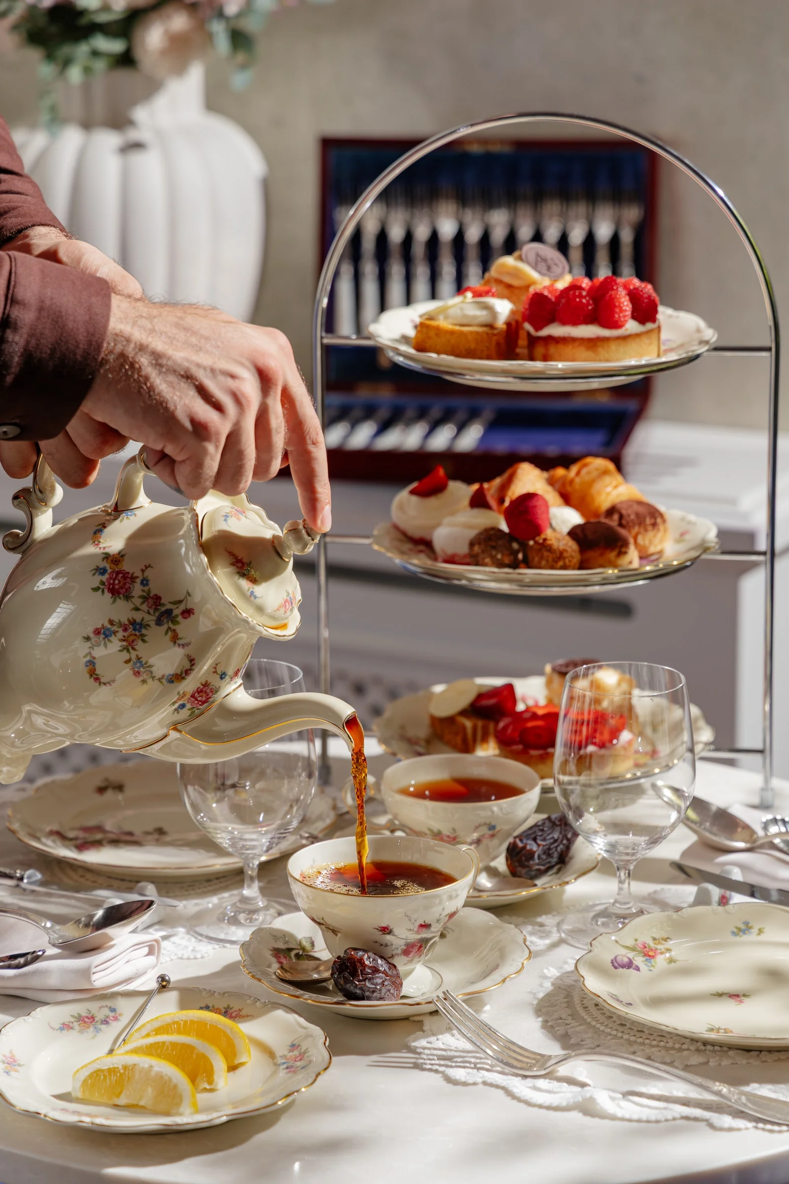 Tea being poured from a floral porcelain teapot next to a stand of desserts