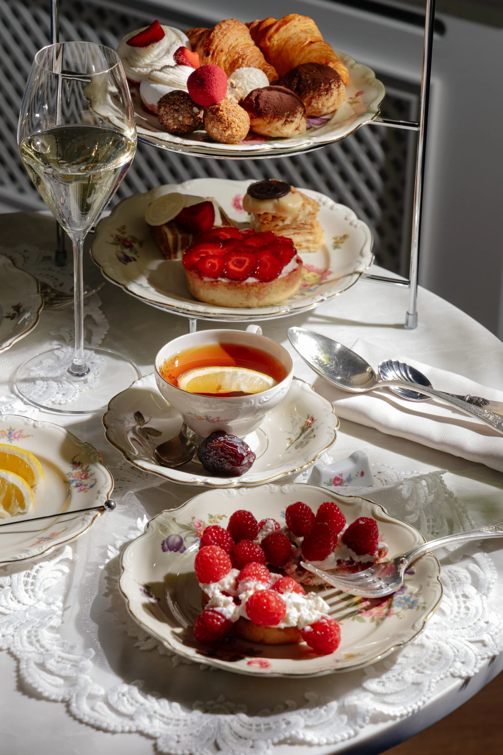 Raspberry tartlet, a cup of tea with lemon and a glass of champagne on a table laid with a lace tablecloth